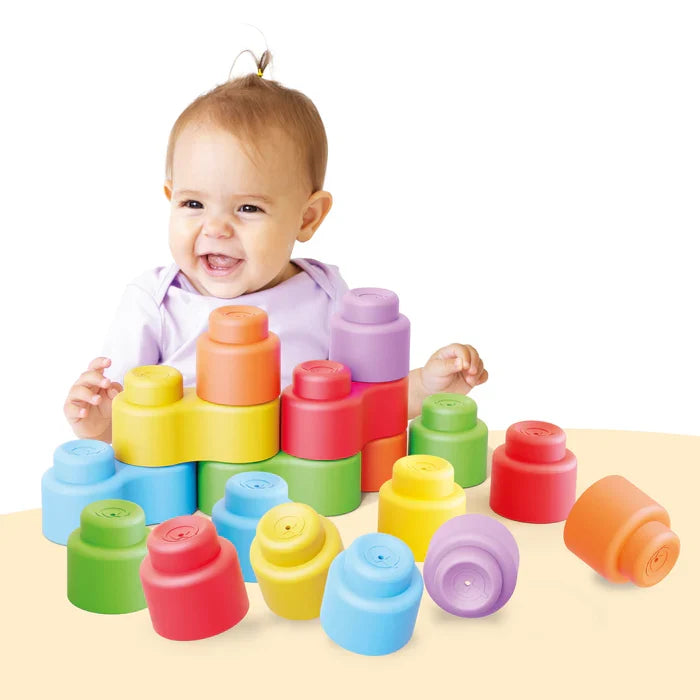 Smiling baby playing with soft, rounded building blocks in pastel blue, green, yellow, orange, and pink.