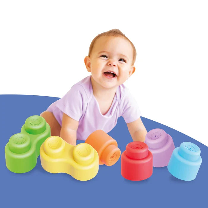 Smiling baby playing with colorful, soft, rounded building blocks in lime, yellow, orange, red, purple, and blue.