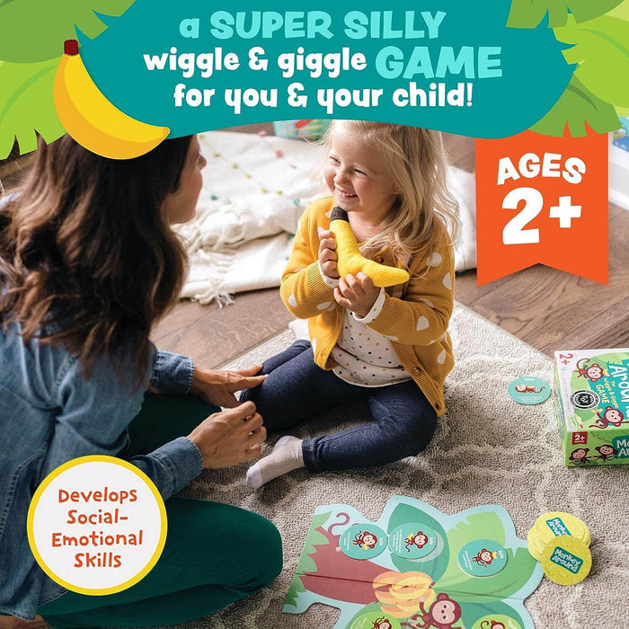 Mother and child play with a yellow plush banana and monkey game cards on a rug. Age 2+ and jungle graphics are visible.