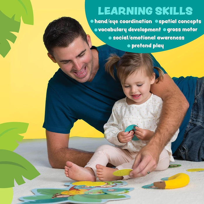 A father and toddler play with round monkey cards, a leaf mat, and a plush banana toy on the floor.