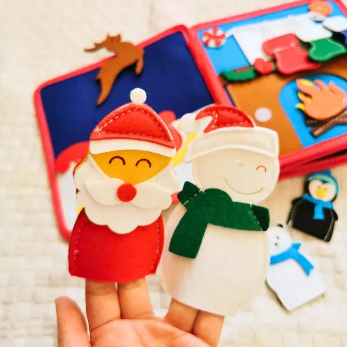 Hand holding Santa and snowman felt finger puppets over an open Christmas busy board book with colorful holiday scenes.