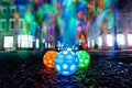 Three glowing, dimpled balls in blue, orange, and green on wet pavement with colorful neon light streaks in the back.