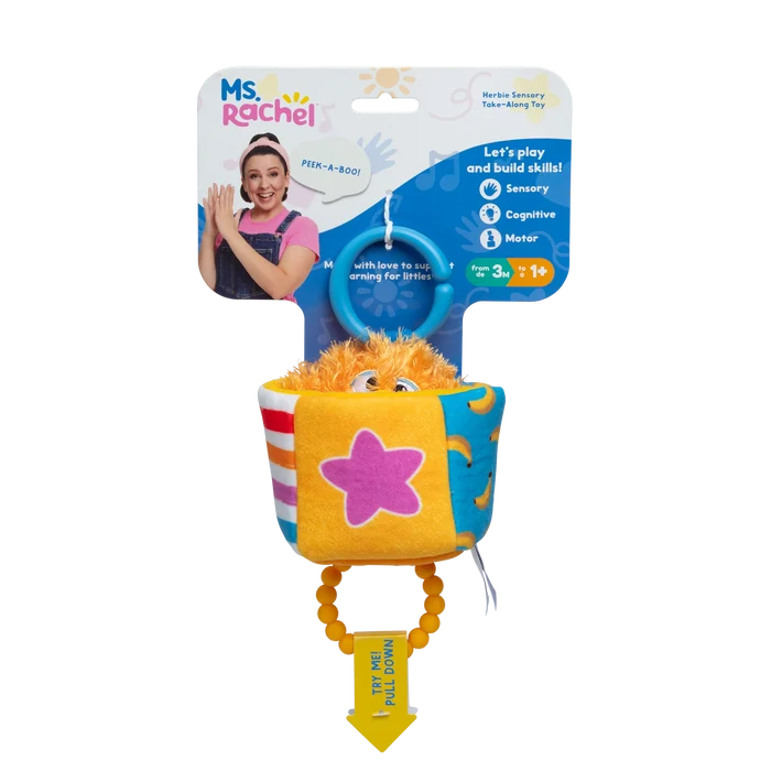 Orange fuzzy toy in a colorful plush cup with a pink star, blue hanging ring, and yellow pull handle on packaging.