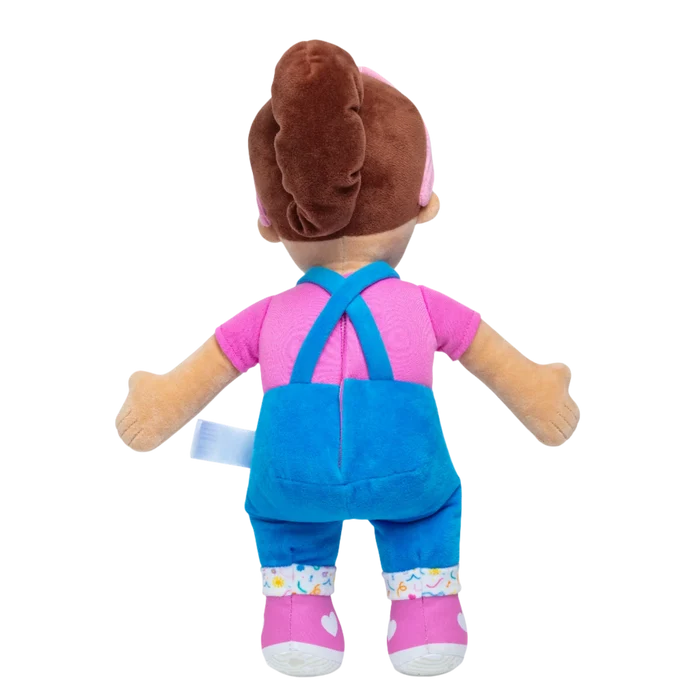 Rear view of a plush doll with a brown ponytail, pink t-shirt, blue overalls, and pink shoes with white hearts.