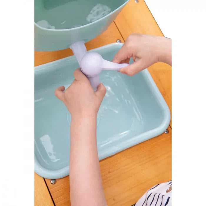Child's hands operating a white plastic water pump over light blue basins in a wooden outdoor play kitchen.