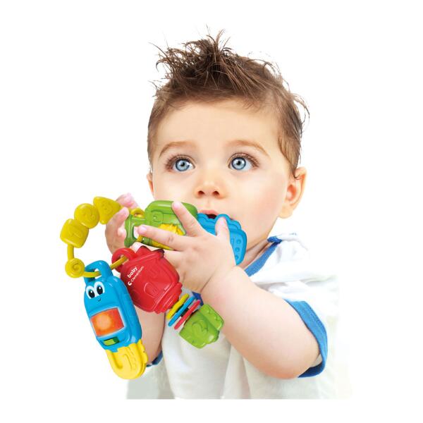 Baby holding colorful plastic toy keys with a light-up blue character, a red car, and textured green surfaces.