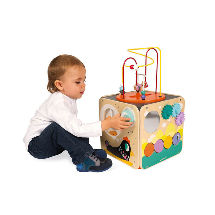 Toddler playing with a wooden activity cube featuring colorful gears, a bead maze top, and animal illustrations.
