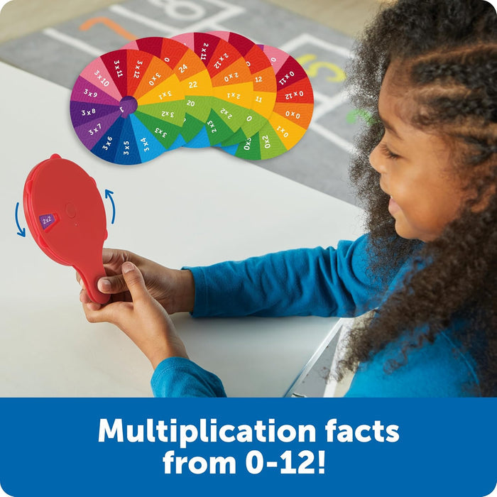 Child holding a red handheld toy showing 2x2, with colorful multiplication fact discs from zero to twelve.