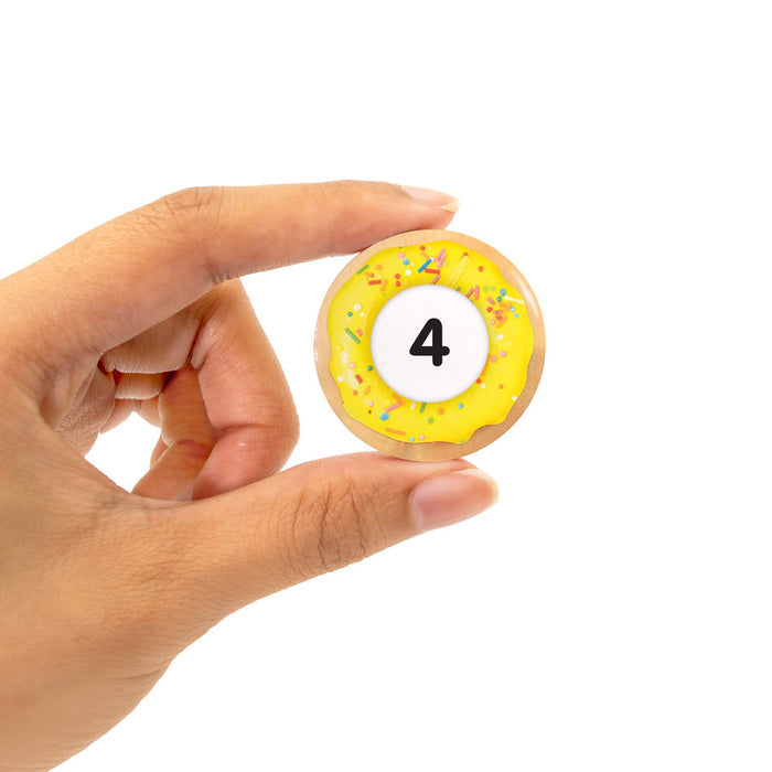 Hand holding a wooden donut-shaped game piece with yellow icing, colorful sprinkles, and the number 4.