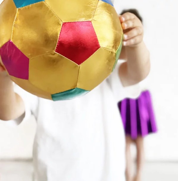 Large, shiny gold fabric soccer ball with colorful metallic panels held by a child in a white shirt.