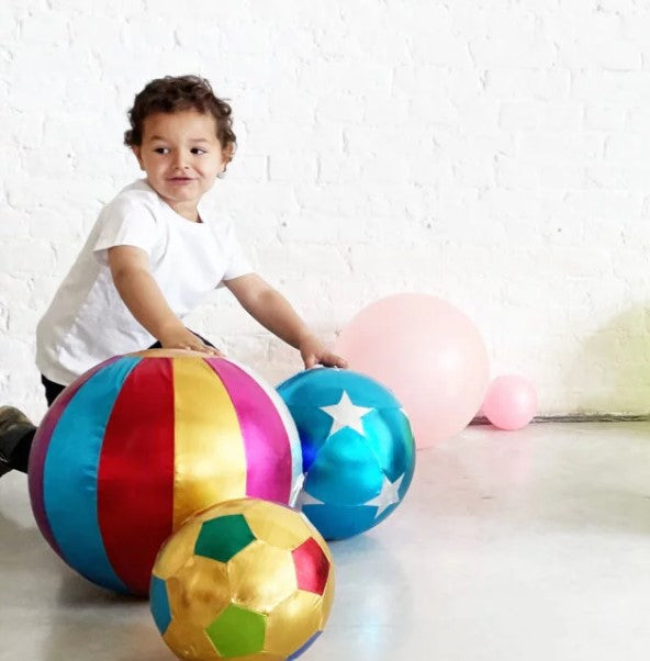 Gold fabric soccer ball with colorful pentagon panels, shown with a child and larger colorful inflatable balls.