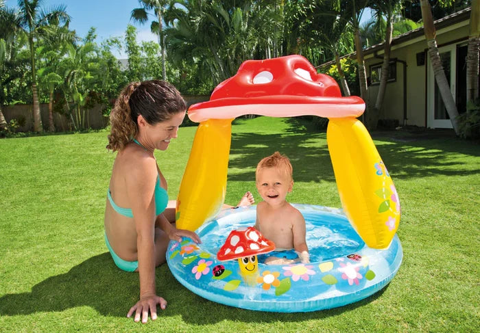 Blue inflatable baby pool with a red mushroom canopy, yellow pillars, and floral prints on a grassy lawn.