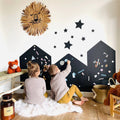 Two children playing with colorful magnets on three black house-shaped magnetic chalkboards on a playroom wall.