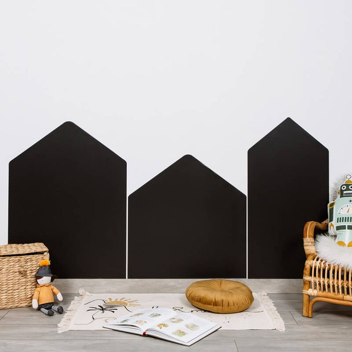 Three black house-shaped magnetic chalkboard wall panels arranged on a white wall in a child's playroom.