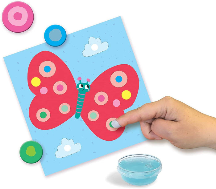 A child's hand finger painting a red butterfly with colorful circular stickers and a bowl of blue paint.