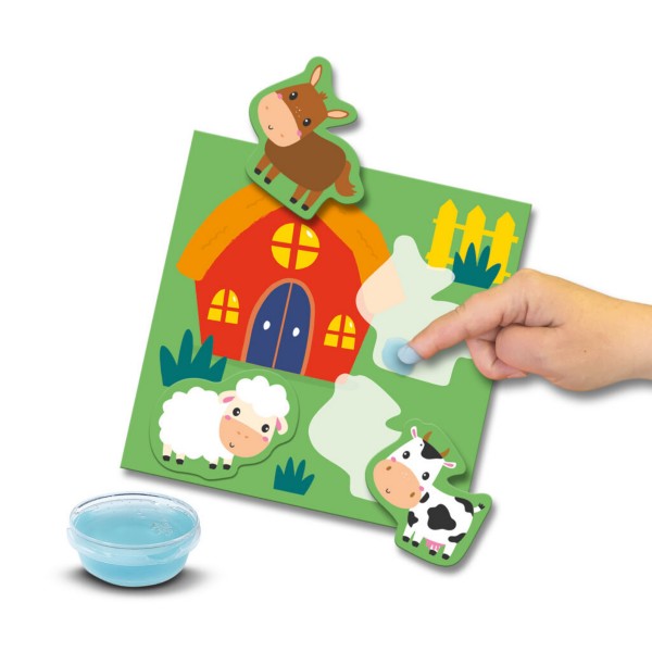 Hand applies blue dough to a barnyard card featuring a red barn, animal shapes, and a small bowl of blue dough.