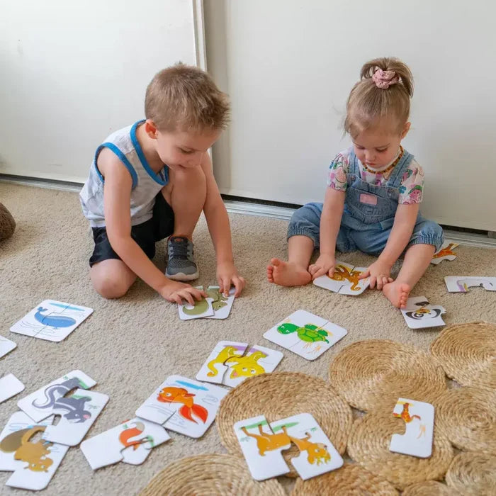 Two children sitting on the floor matching head and tail puzzle pieces featuring colorful animal illustrations.