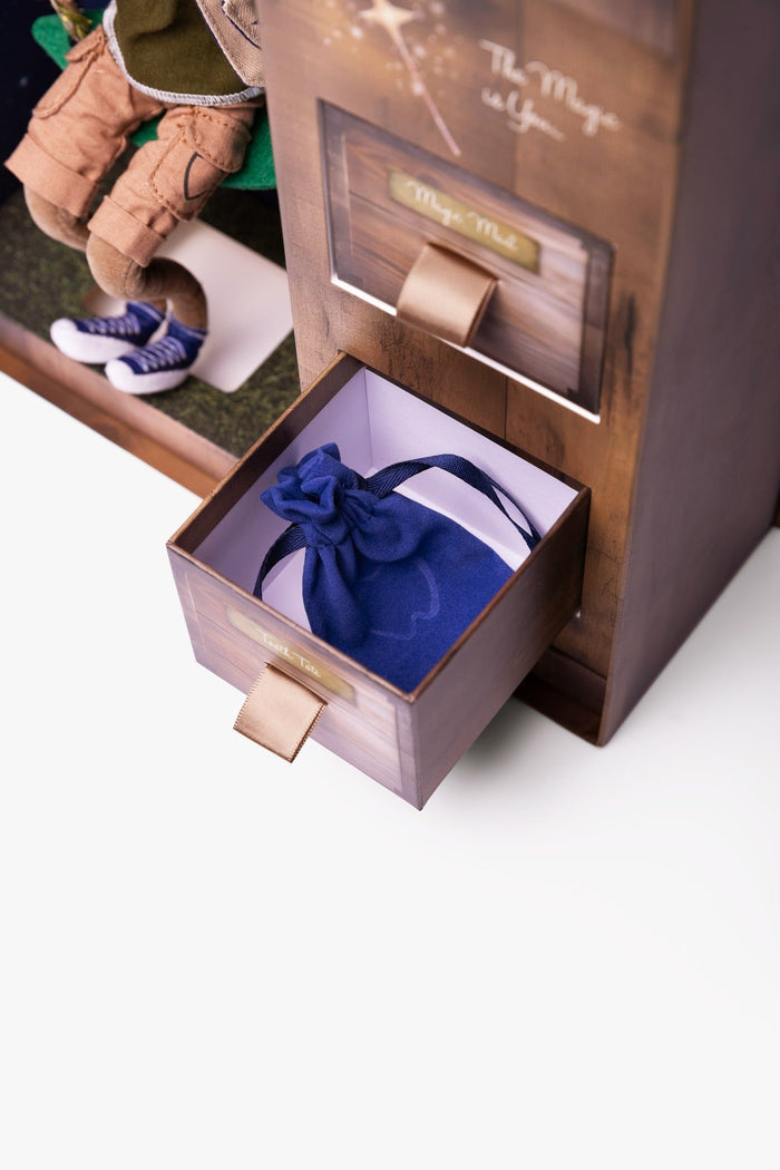 Wooden toy chest with open drawer holding a blue velvet pouch, labeled Tooth Tote, with a boy doll nearby.