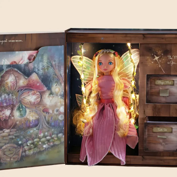 Blonde fairy doll in a pink dress on a lighted swing inside an illustrated wooden book-style box with small drawers.
