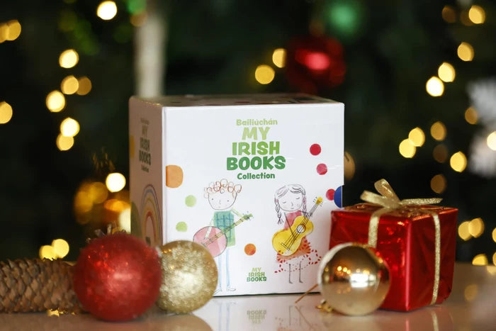 White square box with child illustrations and green text, among red and gold holiday ornaments and a wrapped gift.