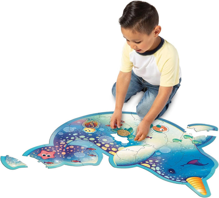A boy assembling a large, blue narwhal-shaped floor puzzle featuring vibrant illustrations of underwater sea creatures.