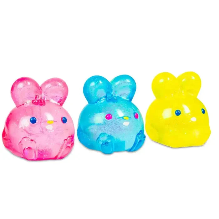 Three glittery, translucent bunny-shaped fidget toys in pink, blue, and yellow with small eyes and noses.
