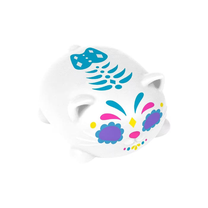 White squishy cat toy with purple eyes, colorful sugar skull face markings, and a blue fish skeleton on its back.