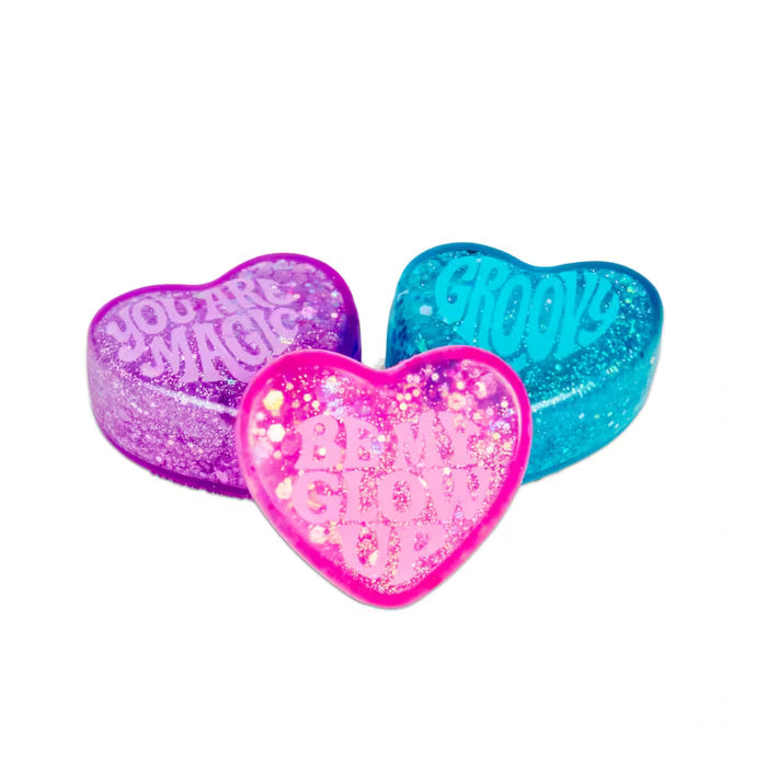 Three sparkly, heart-shaped fidget toys in purple, blue, and pink with text: You Are Magic, Groovy, and Be My Glow Up.