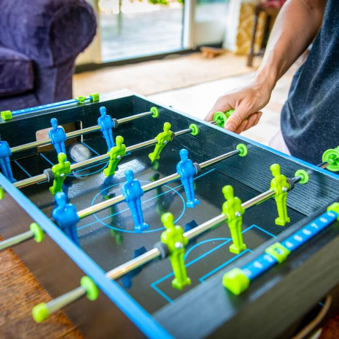 Miniature foosball table with neon blue and green players, silver rods, and a score tracker on a black surface.