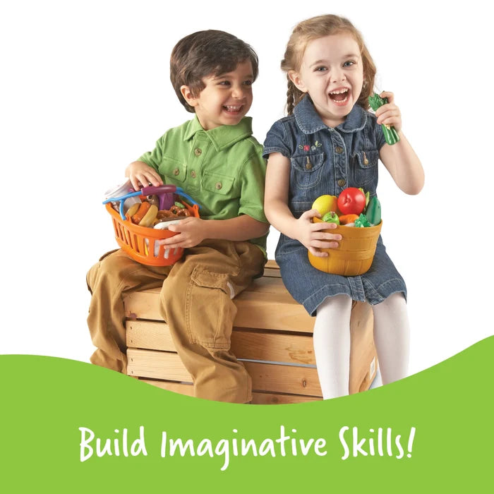 Two laughing children sit on a wooden crate holding baskets of toy food. Green banner reads: Build Imaginative Skills!