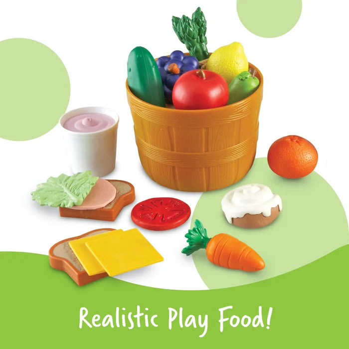 Colorful toy food set with a basket of produce, yogurt cup, carrot, orange, cinnamon roll, and sandwich ingredients.