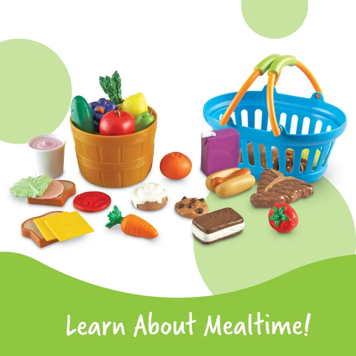 Colorful plastic play food set including fruits, vegetables, snacks, a brown basket, and a blue shopping basket.