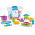 Colorful toy pots, pans, and utensils displayed around a clear plastic storage bin with blue handles.