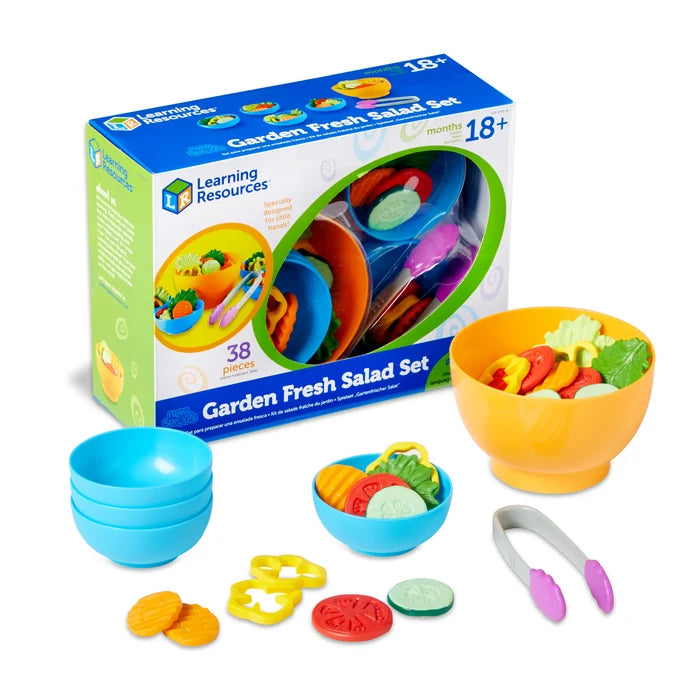 Toy salad set featuring yellow and blue bowls, tongs, and plastic vegetables in front of its blue product box.