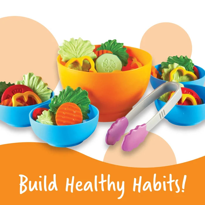 Play food salad set with colorful plastic vegetables in orange and blue bowls with gray and purple tongs.
