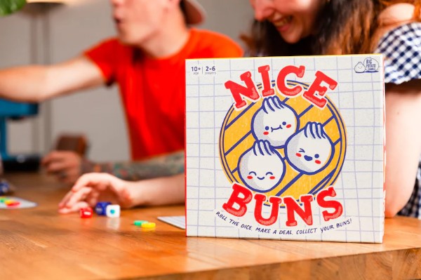 Square board game box featuring three cute cartoon dumplings in a steamer basket and red text on a white grid background.