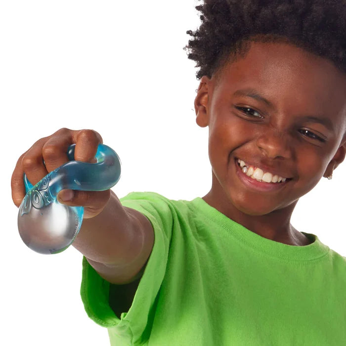 A smiling boy squeezes a translucent blue squishy cube toy, showing its flexible and morphing texture.