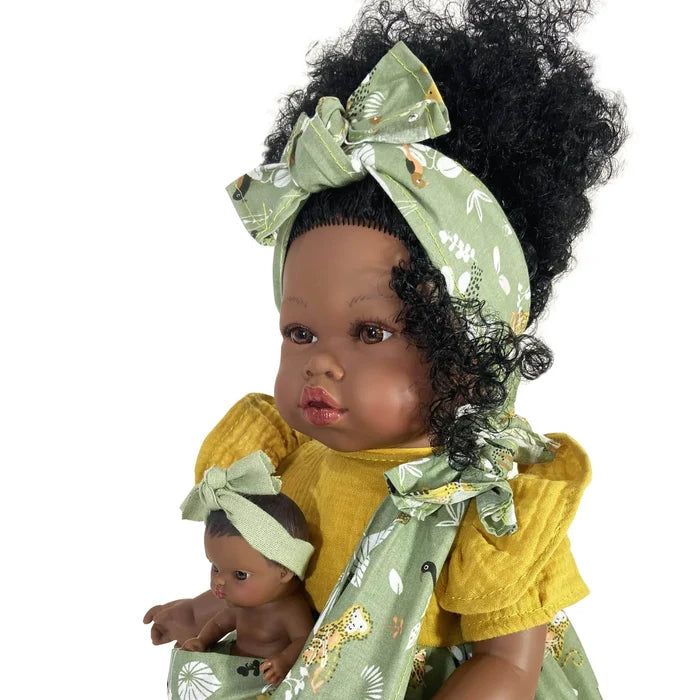 Black baby doll in a yellow dress and green animal-print headband, carrying a tiny doll in a matching sling.