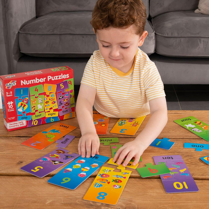 Young boy playing with colorful Galt 3-piece number puzzles on a wooden table near the red product box.