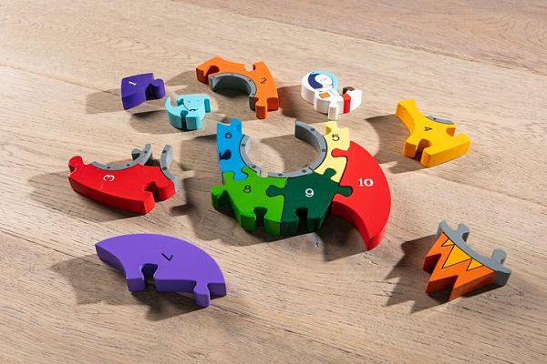 Colorful wooden puzzle pieces with numbers 1 to 10 and an astronaut figure scattered on a light wood floor.