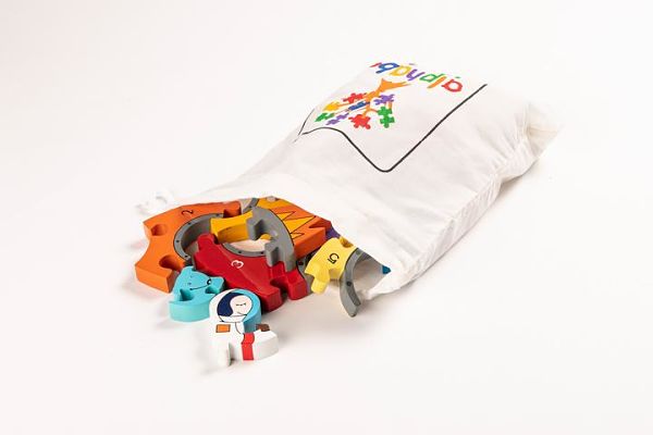 Colorful numbered wooden puzzle pieces with an astronaut illustration spilling out of a white drawstring cloth bag.
