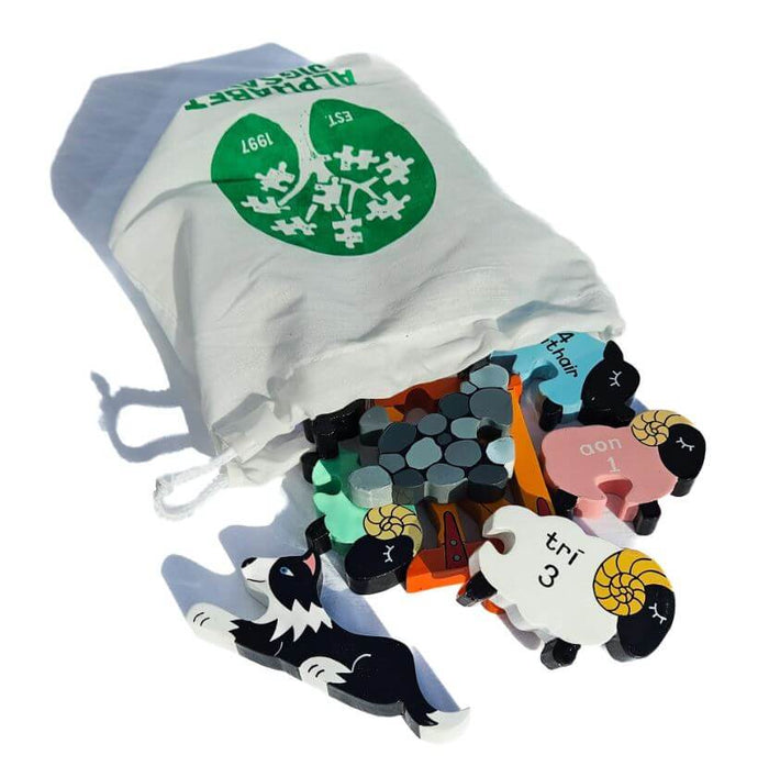 Colorful wooden sheep puzzle pieces with Irish numbers and a sheepdog spilling from a white Alphabet Jigsaws bag.