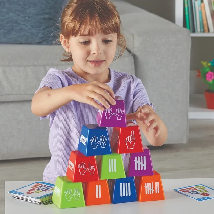 A young girl stacks colorful plastic cups with tally marks, finger counts, and ten-frames into a pyramid.