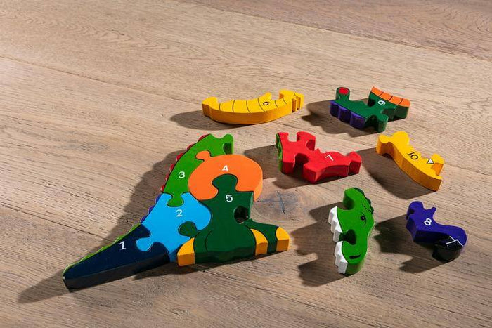 Colorful wooden T-Rex jigsaw puzzle with pieces numbered 1-10, partially assembled on a light wood floor.
