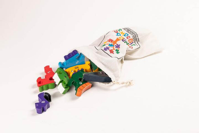 Colorful numbered wooden dinosaur puzzle pieces spilling from a white cloth drawstring bag.