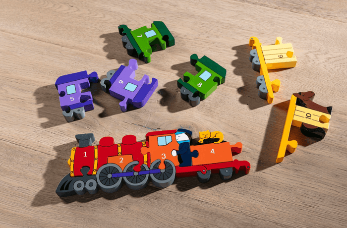 Colorful wooden train puzzle pieces numbered 1-10 on a wood floor, with numbers 1-4 connected as the engine.