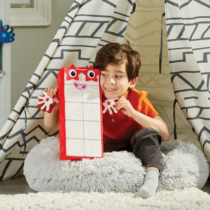 Boy holding a tall rectangular red and white plush toy with a grid pattern, star-shaped glasses, and star hands.