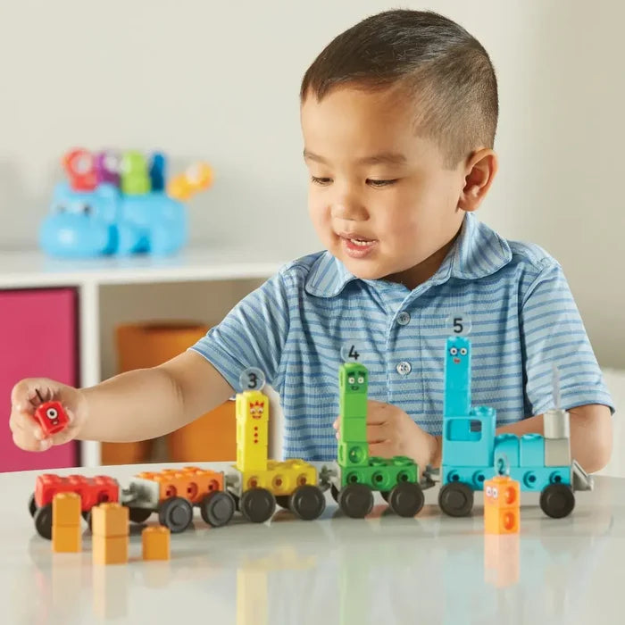 Child building a colorful toy train with numbered blocks 1-5 featuring character faces on a white table.