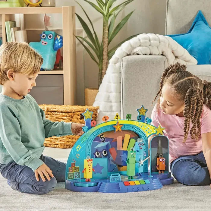 Two children play with a blue musical stage toy featuring colorful Numberblocks figures and a star-topped yellow arch.