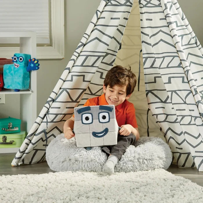 A boy in a patterned teepee holds a smiling gray cube plush toy featuring a 3x3 grid face and blue eyebrows.